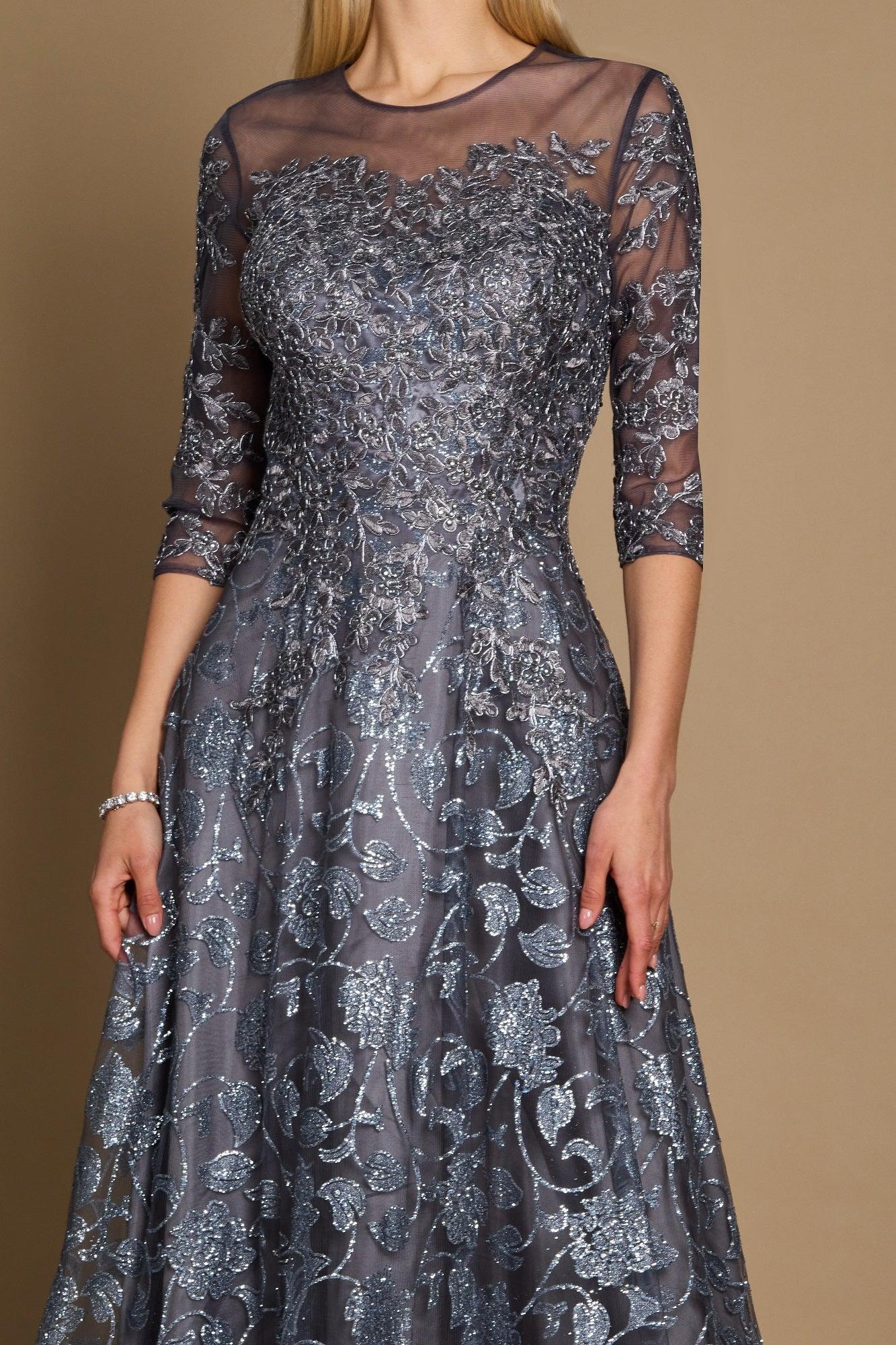 A long formal evening dress in charcoal gray, featuring intricate lace detailing and a flowing silhouette, elegantly draping to the floor.
